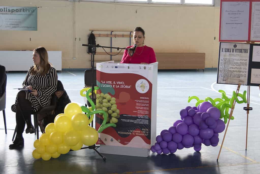 Presentatrice durante evento vitivinicolo con decorazioni di grappoli di uva gialli e viola.